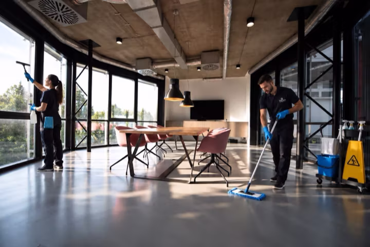 A professional cleaning team washing windows and mopping the floor of a modern office